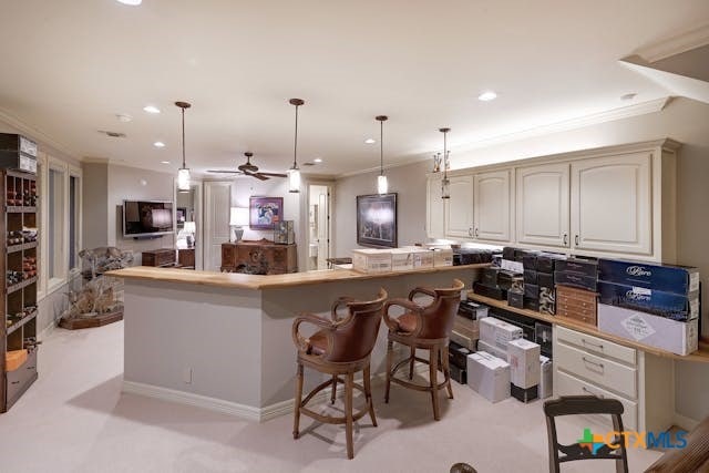 kitchen featuring a breakfast bar area, decorative light fixtures, crown molding, and light colored carpet