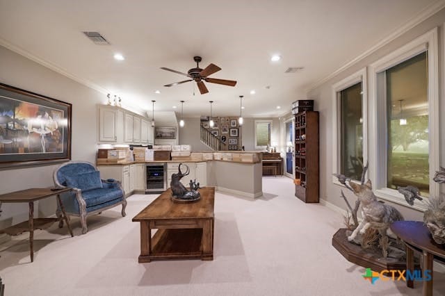 living room featuring wine cooler, ceiling fan, light colored carpet, and ornamental molding