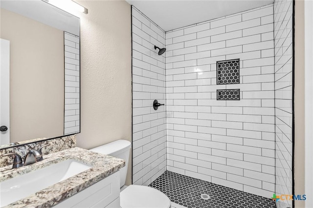 bathroom with vanity, toilet, and a tile shower