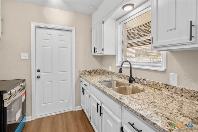 kitchen with sink, stainless steel range with electric cooktop, white cabinets, light stone countertops, and light hardwood / wood-style flooring