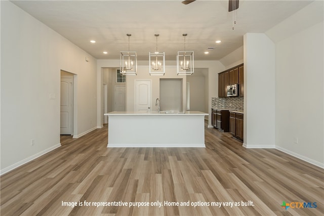 kitchen with dark brown cabinets, light hardwood / wood-style flooring, hanging light fixtures, and an island with sink