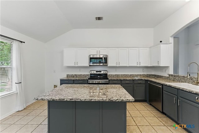 kitchen with appliances with stainless steel finishes, a sink, light tile patterned floors, vaulted ceiling, and white cabinetry