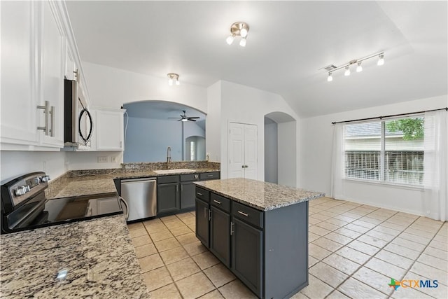 kitchen with appliances with stainless steel finishes, arched walkways, a sink, vaulted ceiling, and light tile patterned flooring