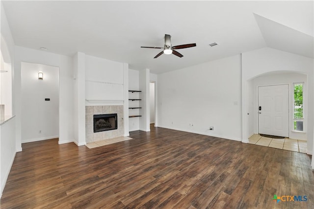 unfurnished living room featuring a ceiling fan, wood finished floors, a tiled fireplace, and baseboards