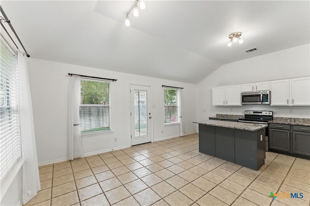 kitchen with appliances with stainless steel finishes, vaulted ceiling, a center island, light tile patterned floors, and healthy amount of natural light