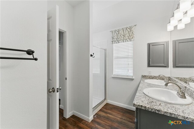bathroom with a shower stall, wood finished floors, baseboards, and double vanity