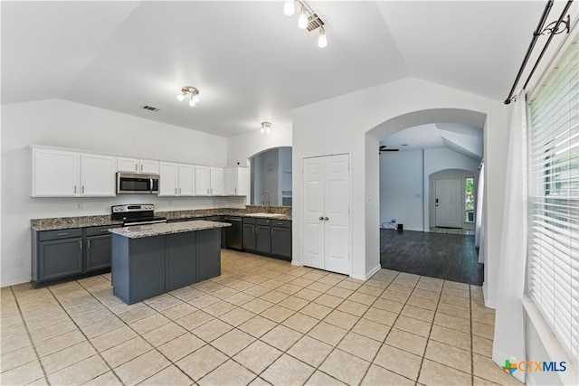 kitchen featuring vaulted ceiling, stainless steel appliances, a kitchen island, white cabinets, and light tile patterned flooring