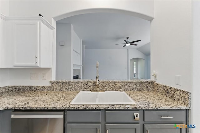 kitchen with gray cabinetry, dishwasher, a sink, a ceiling fan, and arched walkways