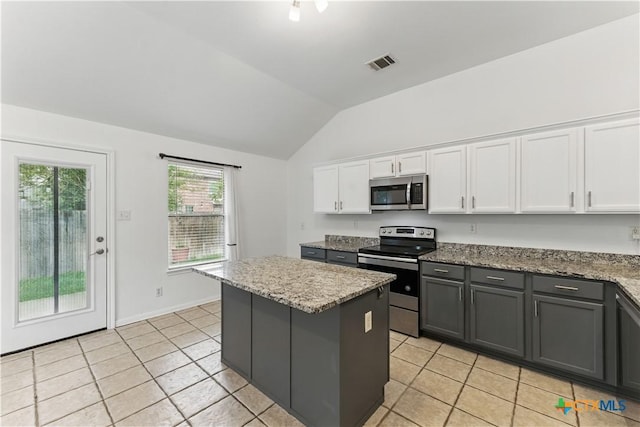 kitchen with appliances with stainless steel finishes, lofted ceiling, light tile patterned floors, white cabinets, and a kitchen island