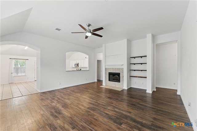 unfurnished living room with ceiling fan, dark wood-style flooring, a fireplace, arched walkways, and vaulted ceiling