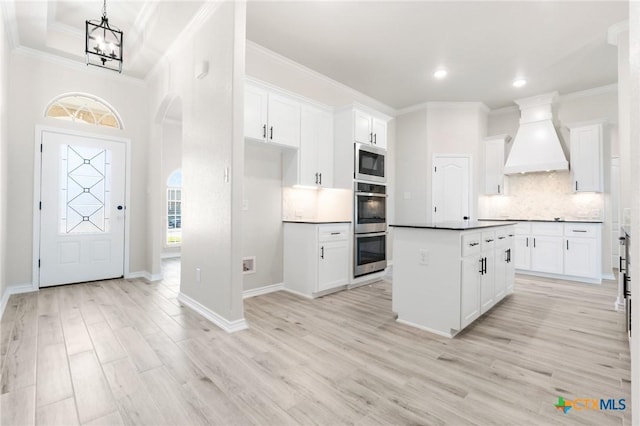 kitchen featuring white cabinetry, crown molding, stainless steel appliances, and custom range hood