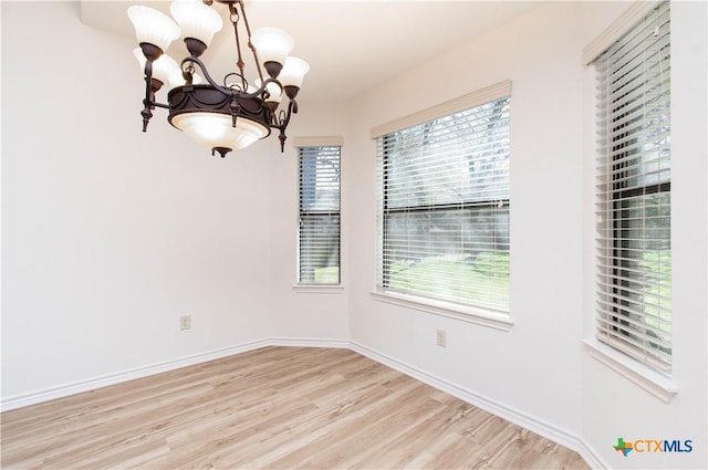 spare room featuring light wood-style floors, baseboards, and a notable chandelier