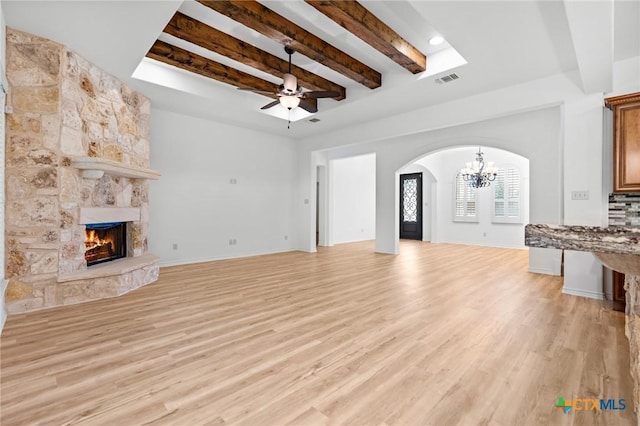 1010 Woodland Bend Cir, Salado, TX 76571 - unfurnished living room featuring a chandelier, beamed ceiling, arched walkways, a stone fireplace, and light wood-style floors