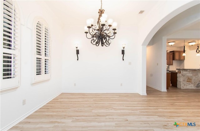 unfurnished dining area with visible vents, arched walkways, light wood-style floors, an inviting chandelier, and baseboards