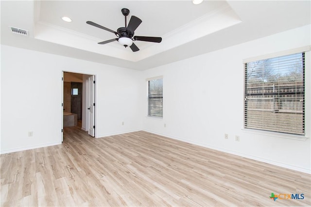 empty room featuring a raised ceiling, light wood-style flooring, visible vents, and ornamental molding