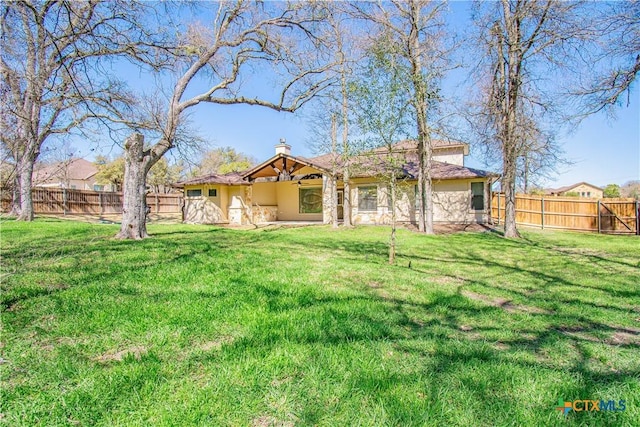 back of property featuring a fenced backyard, stucco siding, a chimney, and a yard