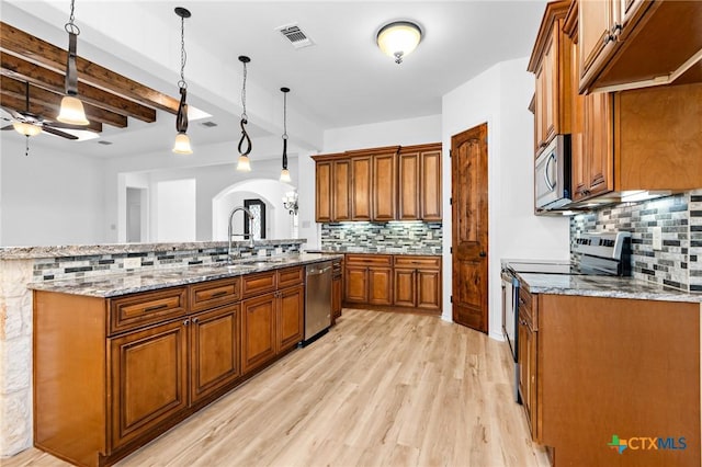 1010 Woodland Bend Cir, Salado, TX 76571 - kitchen with stainless steel appliances, brown cabinetry, decorative backsplash, arched walkways, and ceiling fan