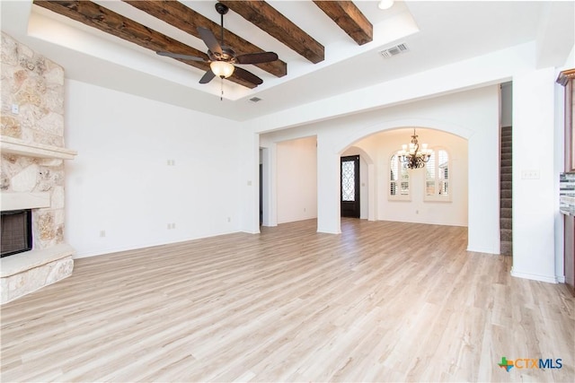 unfurnished living room featuring light wood finished floors, arched walkways, a stone fireplace, beamed ceiling, and ceiling fan with notable chandelier