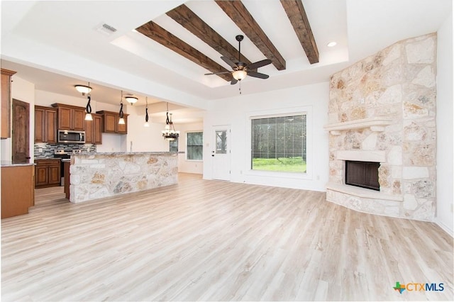 unfurnished living room with visible vents, beamed ceiling, light wood-style flooring, ceiling fan with notable chandelier, and a stone fireplace