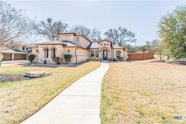 mediterranean / spanish-style house featuring stucco siding, stone siding, a front lawn, and fence