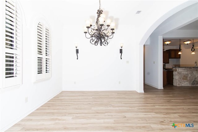 unfurnished dining area featuring visible vents, baseboards, wood finished floors, arched walkways, and a notable chandelier