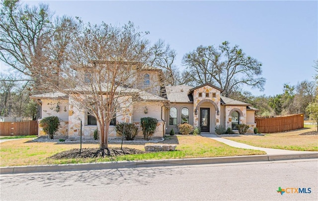 mediterranean / spanish-style home with stone siding, a front yard, and fence