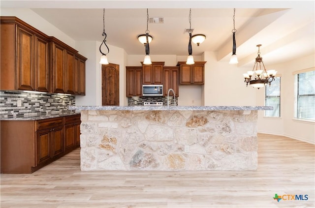 kitchen featuring light wood finished floors, stainless steel microwave, visible vents, and decorative backsplash