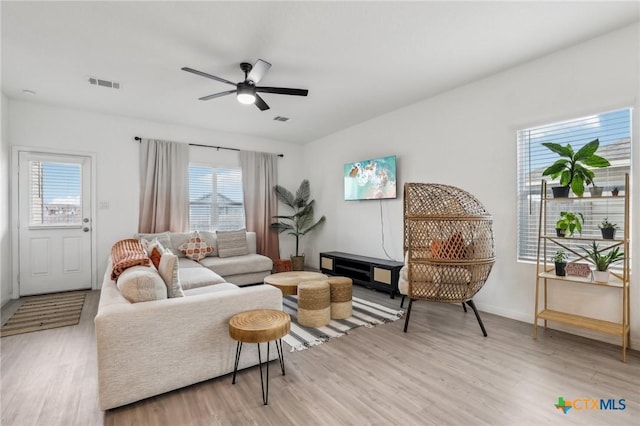 living room featuring baseboards, light wood finished floors, visible vents, and a ceiling fan