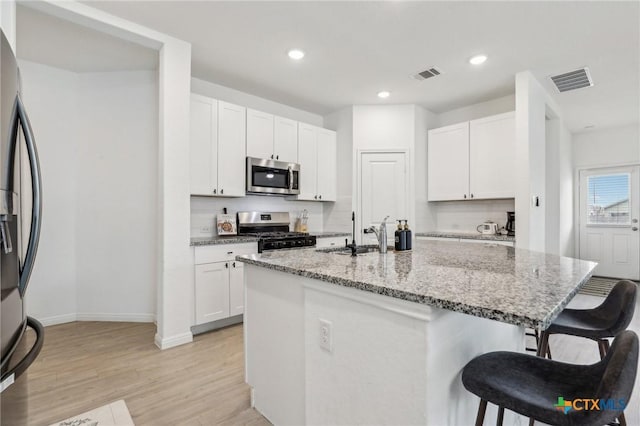 kitchen with light stone counters, a breakfast bar area, stainless steel appliances, visible vents, and a sink