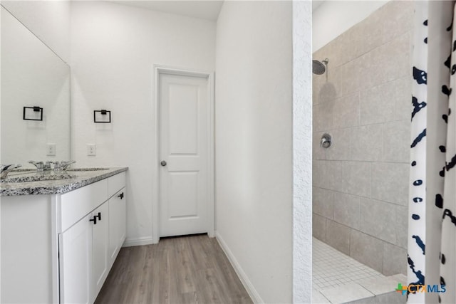 bathroom with tiled shower, wood finished floors, vanity, and baseboards