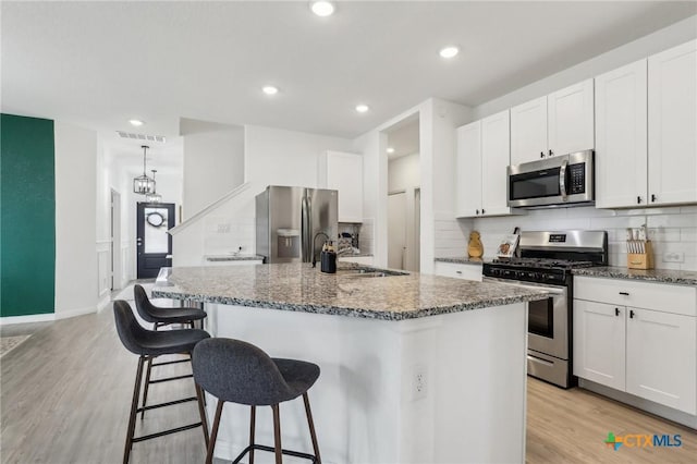 kitchen featuring stainless steel appliances, visible vents, stone countertops, light wood-style floors, and a sink