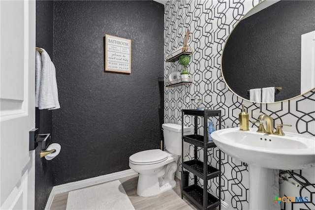 bathroom with baseboards, a textured wall, toilet, wood finished floors, and a sink