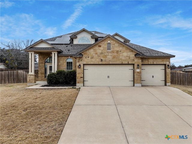 view of front of house featuring a garage, solar panels, a shingled roof, fence, and driveway