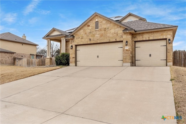 view of front facade with a garage, driveway, a shingled roof, solar panels, and fence