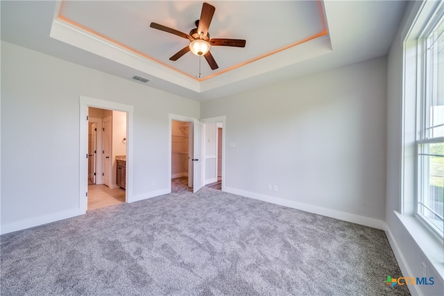 unfurnished bedroom with ensuite bath, a spacious closet, ceiling fan, and a raised ceiling