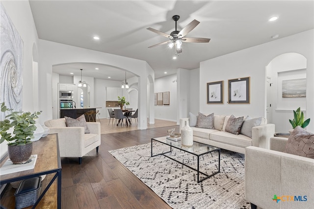 living area with ceiling fan, recessed lighting, arched walkways, and dark wood-style floors