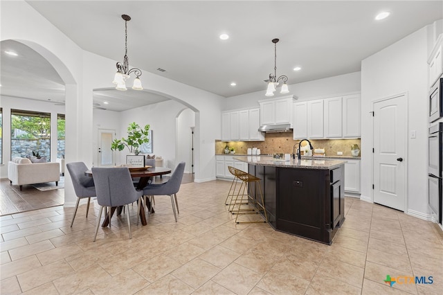 kitchen featuring light stone counters, recessed lighting, backsplash, white cabinets, and under cabinet range hood