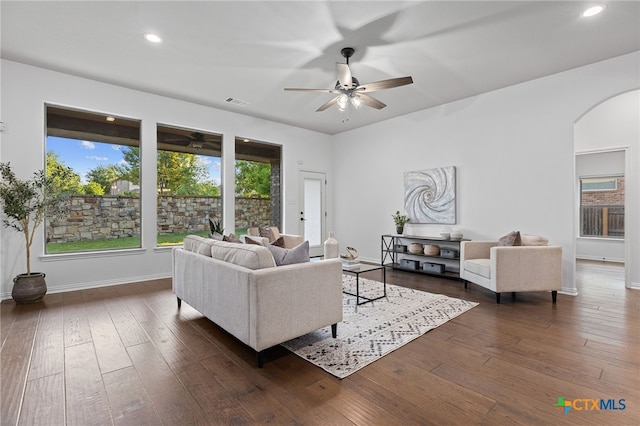 living room with arched walkways, baseboards, a ceiling fan, and dark wood finished floors
