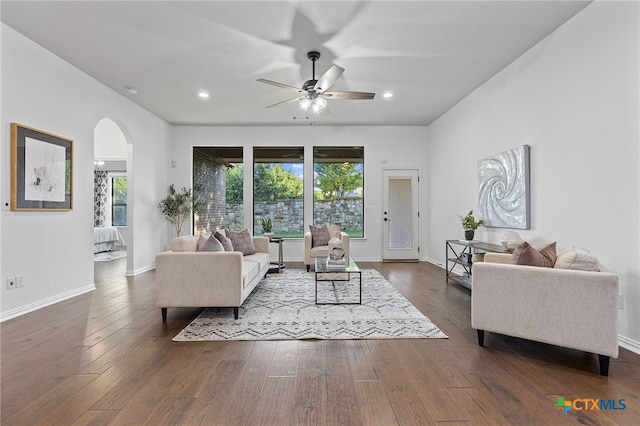 living room with a wealth of natural light, arched walkways, dark wood-type flooring, and ceiling fan