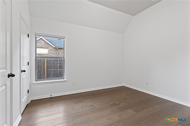 unfurnished room featuring dark wood-style flooring, baseboards, and vaulted ceiling