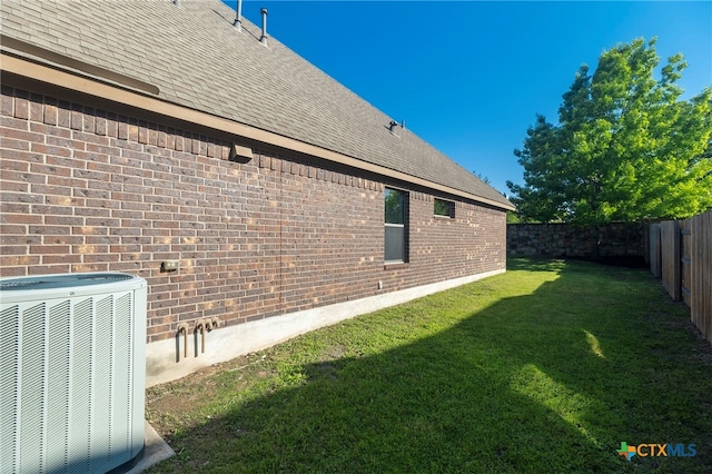 view of side of property with a yard, roof with shingles, central AC, and a fenced backyard