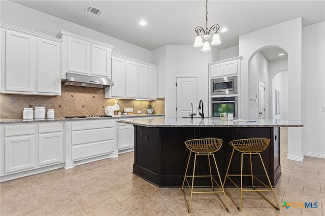 kitchen featuring tasteful backsplash, appliances with stainless steel finishes, under cabinet range hood, white cabinetry, and light stone countertops