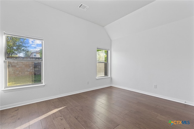 spare room with dark wood-type flooring, visible vents, baseboards, and vaulted ceiling