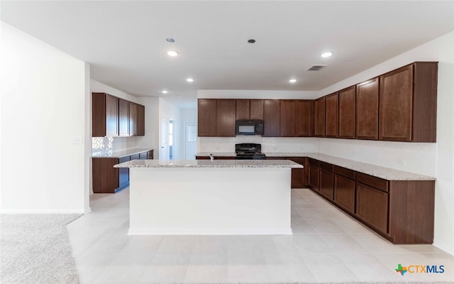 kitchen featuring light stone counters, dark brown cabinetry, black appliances, and a center island