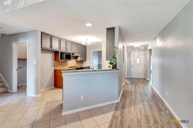 kitchen with light hardwood / wood-style flooring, a textured ceiling, light stone counters, and gray cabinetry