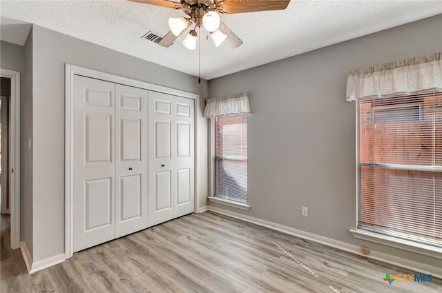 unfurnished bedroom featuring ceiling fan, a textured ceiling, a closet, and light hardwood / wood-style flooring