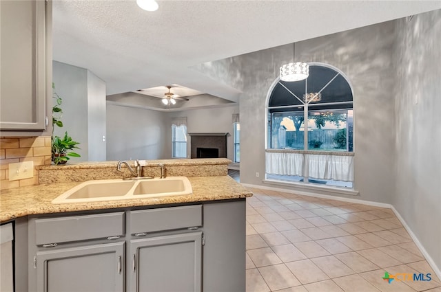 kitchen with ceiling fan with notable chandelier, kitchen peninsula, a textured ceiling, sink, and gray cabinetry