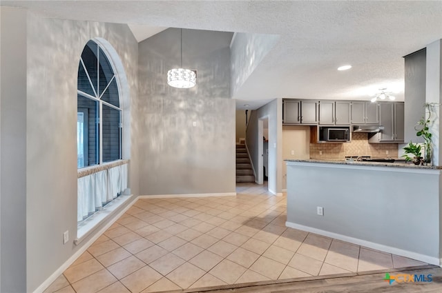 kitchen with light tile patterned floors, a textured ceiling, gray cabinets, light stone countertops, and decorative light fixtures