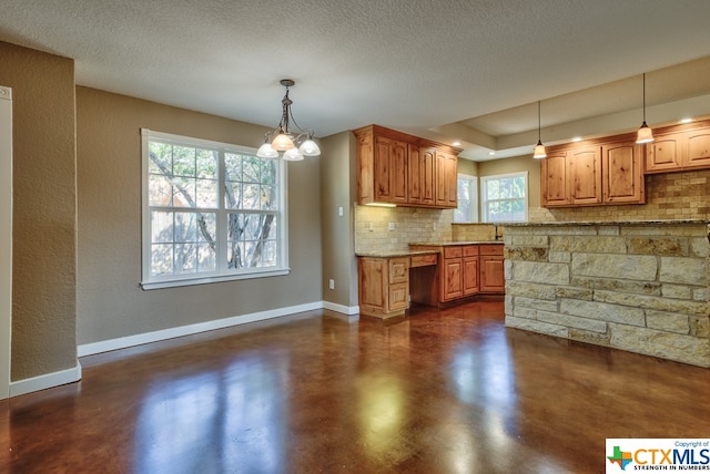 kitchen with hanging light fixtures, a wealth of natural light, light stone counters, and tasteful backsplash