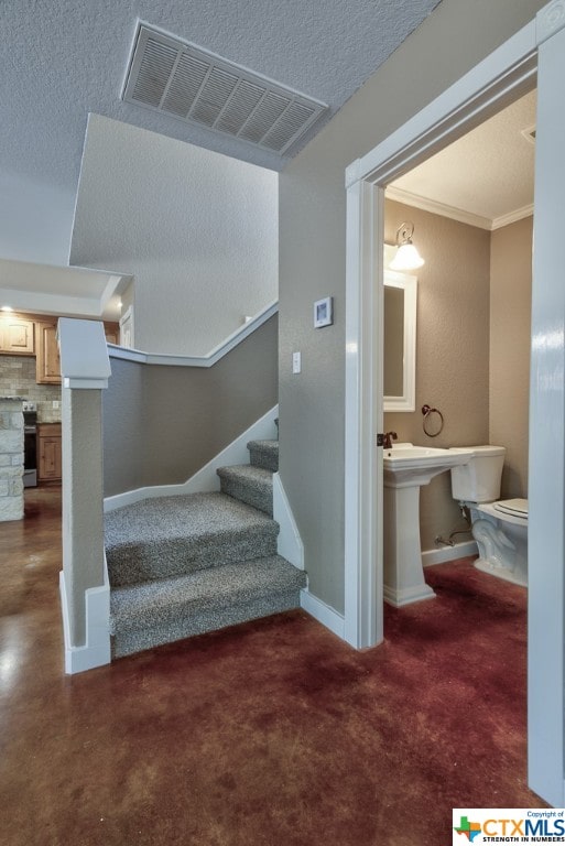 staircase featuring a textured ceiling, carpet flooring, and crown molding